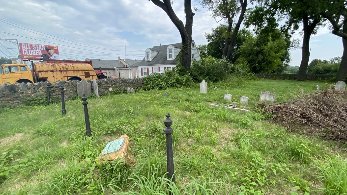 The Carter Graveyard in 2023: rough grass, scattered low stones and a stone wall along Concord Road