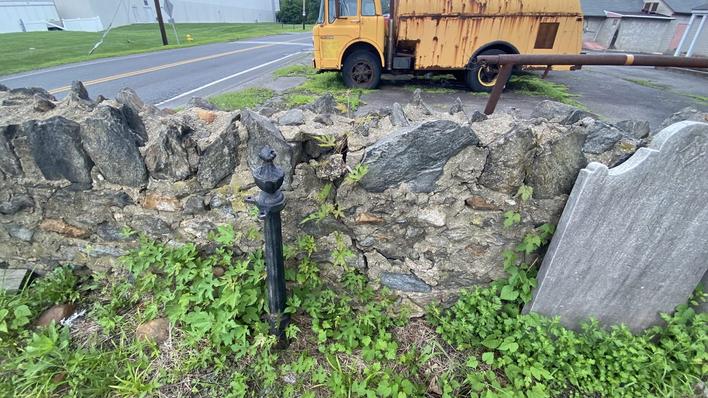 Several old headstones leaning against the broken stone wall beside Concord Road