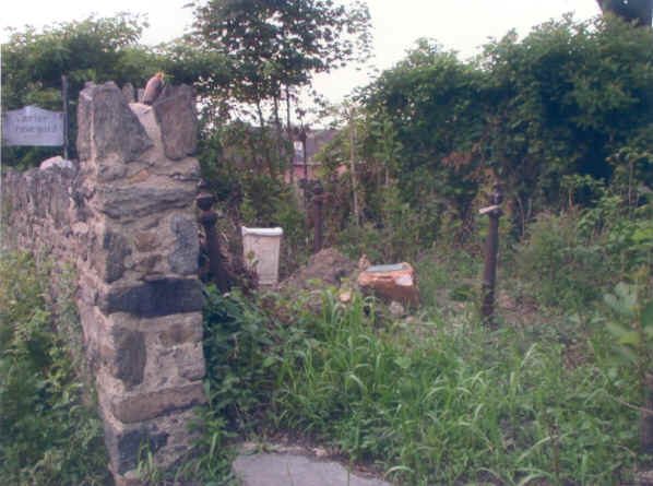 Broken stone wall and gate pier at the graveyard entrance, overgrown with brush